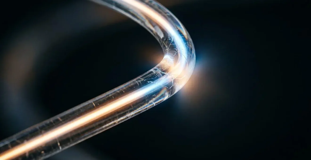 Macro photograph showing light refraction through curved glass fiber demonstrating total internal reflection failure at a sharp bend